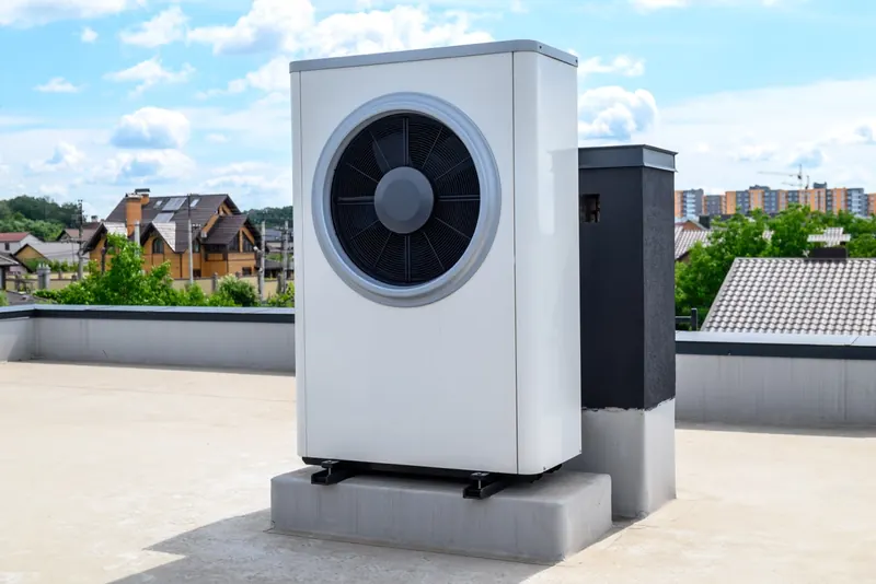 Buitenunit van een warmtepomp op een plat dak, met woningen op de achtergrond
